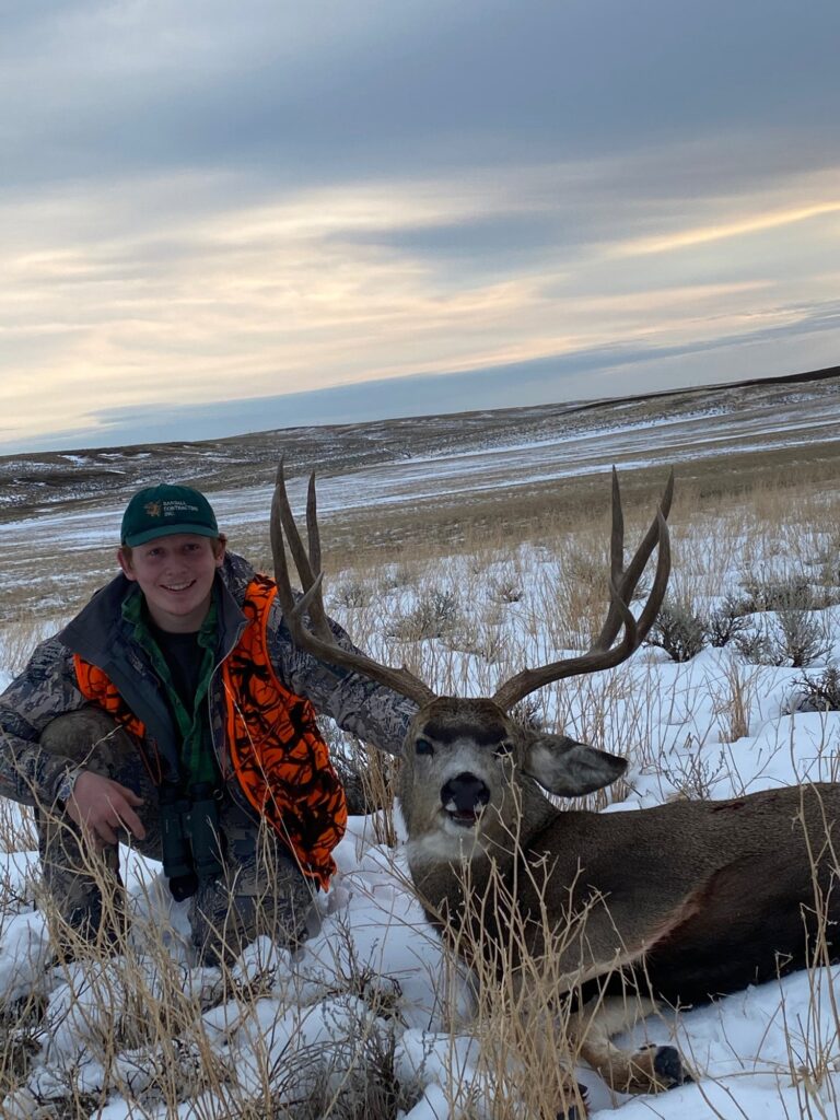 Young hunter in a field with snow kneeling next to deer