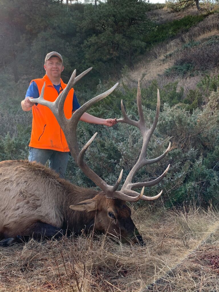 Man Standing in front of large hill holding large deer antlers